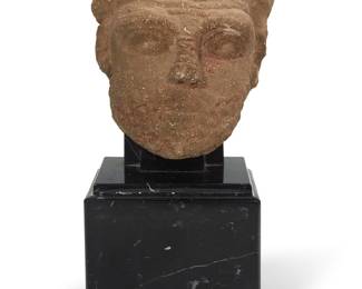 105 A Roman/Coptic carved limestone head of a faun Circa 200-600 CE With horns, curly hair, pronounced eyes, and short beard, mounted on an armature, raised on a black marble base with rotating base Height 7 in., width 6 1/2 in., depth 3 7/8 in.; height of base 11 3/4 in., width 5 5/8 in., depth 4 3/4 in. Estimate: $800 - $1,200