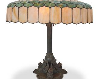 243 A Handel bronze lamp and A. H. Freeman leaded glass shade Early 20th century The pedestal base with three winged lions and a columnar standard issuing three Hubbell lights surmounted by a leaded slag glass shade, electrified Base marked to underside: HANDEL / 1953; shade marked: A. H. FREEMAN Height of lamp 25 3/4 in., width 11 1/4 in., depth 10 in.; height of shade 7 7/8 in., diameter 23 3/4 in. Estimate: $1,000 - $1,500