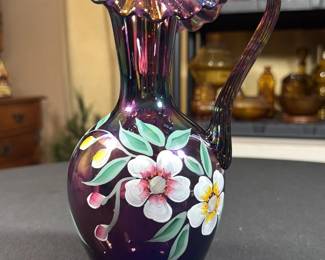 Signed Fenton hand-painted iridescent purple carnival glass pitcher featuring a ruffled crest rim and floral motif
