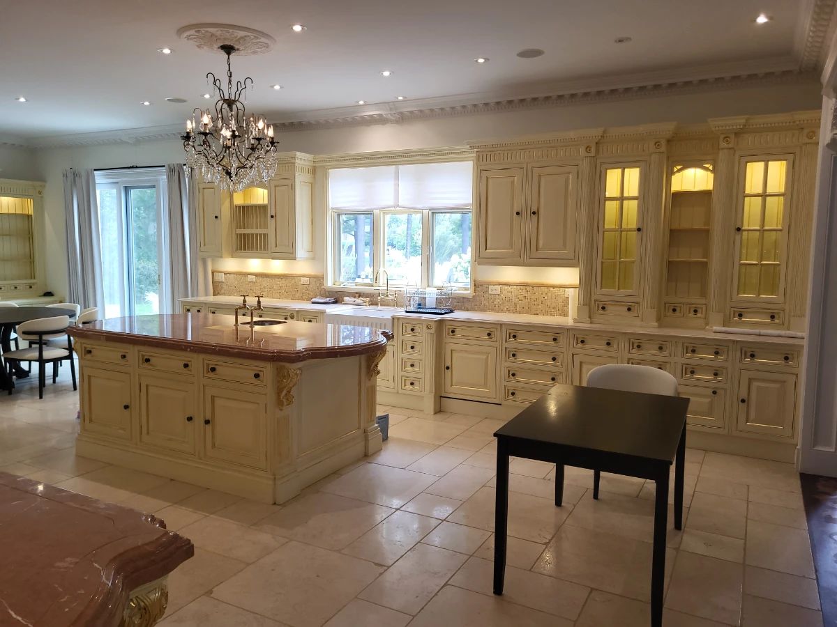 $49,500. Approximately 900 sq. ft. kitchen / breakfast / pantry / professional prep installation Estimated original retail / replacement cost: $300,000+ ~60 linear feet total: main run, large island, and pantry/dressing built-ins Cream painted cabinetry with gold-leaf detailing, fluted columns, dentil crown, leaded-glass uppers Includes stone island top (rouge/marble), backsplash tile, Drop front sink, and bridge faucet Built-in appliances INCLUDED and confirmed working: custom wood vent hood; panel-front fridge & freezer; Blue Star grill, cooktop and salamander; and 2 Miele dishwashers Three crystal chandeliers included. Counter stools shown are NOT confirmed included