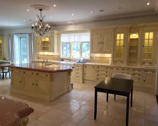 $49,500. Approximately 900 sq. ft. kitchen / breakfast / pantry / professional prep installation Estimated original retail / replacement cost: $300,000+ ~60 linear feet total: main run, large island, and pantry/dressing built-ins Cream painted cabinetry with gold-leaf detailing, fluted columns, dentil crown, leaded-glass uppers Includes stone island top (rouge/marble), backsplash tile, Drop front sink, and bridge faucet Built-in appliances INCLUDED and confirmed working: custom wood vent hood; panel-front fridge & freezer; Blue Star grill, cooktop and salamander; and 2 Miele dishwashers Three crystal chandeliers included. Counter stools shown are NOT confirmed included