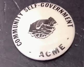 White Pinback Button Featuring The Text "COMMUNITY SELF-GOVERNMENT - ACME" And A Handshake Graphic