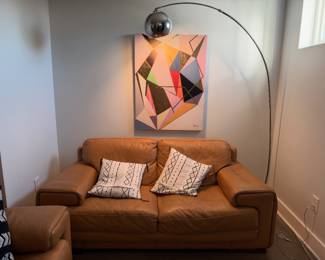 Cognac leather loveseat with arched floor lamp and abstract art