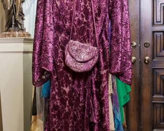 LOT 57 – Elegant Burgundy Cut Velvet Evening Gown with Matching Handbag. A stunning burgundy cut velvet full-length evening gown featuring a gorgeous fleur-de-lis design throughout, elegant long trumpet sleeves, and graceful, shapely pleating at the hem. The rich velvet and intricate detailing give this gown a beautifully dramatic and timeless presence. The ensemble includes a matching satin handbag, adorned with exquisite hand-sewn fleur-de-lis beadwork and finished with a delicate satin rope shoulder strap. An elegant statement gown, perfect for making a memorable impression at any special occasion. Designed by famous fashion and costume designer Margi Kent. Sold as a full ensemble set. • Approx. Size ~8 to 8/10; Approx. Measurements: Waist: 30”, Bust: 36, Hips: 36. • Owner’s note: the gowns can be adjusted in size; there is plenty of fabric in the seams.