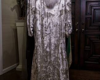 LOT 63 – Gorgeous Silver and White Cut Velvet Evening Gown & White Fox-Trimmed Ensemble. A breathtaking silver and white cut velvet evening gown featuring intricate silver thread and patterning, accented by luxurious white stand-up fox fur trim along the collar and hood. The hood lifts into a dramatic full cascade framing the wearer’s face, creating an exceptionally elegant and distinctive effect. The back of the gown gathers into a graceful mini-train, allowing the fabric to flow beautifully behind. The ensemble includes a heavy matching brocade stole, finished with exquisite white fox fur trim to complement the gown. Designed by famous fashion and costume designer Margi Kent. Sold as a full ensemble set. • Approx. Size ~8 to 8/10; Approx. Measurements: Waist: 30”, Bust: 36, Hips: 36. • Owner’s note: the gowns can be adjusted in size; there is plenty of fabric in the seams.