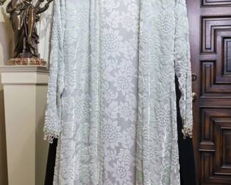 LOT 59 – Elegant Pale Sage Green Velvet & Silk Evening Ensemble. A sophisticated pale sage green cut-velvet evening overdress, styled like an elegant open coat and accented with sparkling crystal embellishments along the hem and cuffs. It is beautifully layered over a pale green silk chiffon mid-calf skirt, featuring a graceful rounded, tiered and gathered hem, cut asymmetrically to one side for a dramatic and subtly alluring leg-baring effect. Designed by famous fashion and costume designer Margi Kent. Sold as a full ensemble set. • Approx. Size ~8 to 8/10; Approx. Measurements: Waist: 30”, Bust: 36, Hips: 36. • Owner’s note: the gowns can be adjusted in size; there is plenty of fabric in the seams.