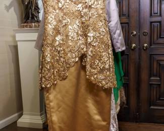 LOT 54 – Exquisite Gold Silk Satin Evening Gown, with French Lace, Embellished with Beads and Sequins, & Ensemble. A stunning gold silk satin evening gown featuring exquisite French lace, hand-sewn gold beads in fleur-de-lis designs, and shimmering sequin and beaded embellishments on the bodice. When buttoned, the back creates an elegant bustle-back appearance; when unbuttoned, it reveals a dramatic, full-length French lace train, giving the gown an almost regal, royal impression. The gown features a long silk satin skirt and versatile cap sleeves that can be worn at mid-elbow length. Designed by famous fashion and costume designer Margi Kent. Sold as a full ensemble set. • Approx. Size ~8 to 8/10; Approx. Measurements: Waist: 30”, Bust: 36, Hips: 36. • Owner’s note: the gowns can be adjusted in size; there is plenty of fabric in the seams.