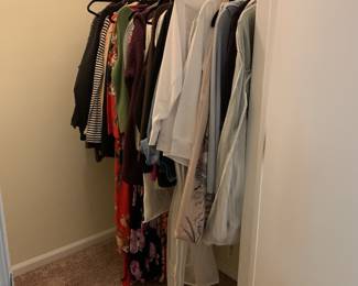 Assorted women's clothing, including sweaters, dresses, and tops, hanging on a closet rod.