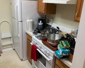 Frigidaire white top-freezer refrigerator and matching gas range, surrounded by oak kitchen cabinetry and various small kitchen appliances and cookware.