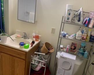 Bathroom vanity with sink, medicine cabinet, and metal shelving unit holding various toiletries, a Conair fabric steamer, and a boxed Conair Halo makeup mirror.