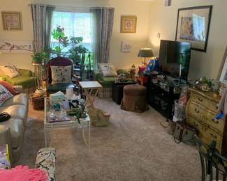 Eclectic living room featuring a variety of furniture, including a leather sofa, green armchairs, a glass-top coffee table, and a vintage-style painted chest of drawers.