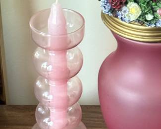Pink glass stacked bubble candle holder holding a matching taper candle, displayed alongside a frosted pink vase topped with a floral ceramic accent.