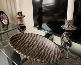 Hand-carved wooden bowl with a zebra stripe pattern, flanked by a pair of African-style carved soapstone candlesticks holding white taper candles.