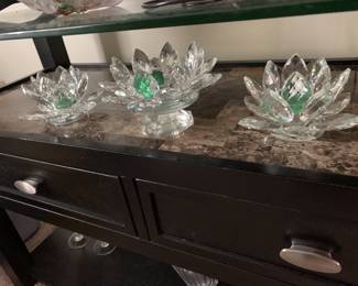 Three faceted crystal lotus flower candle holders, including one elevated on a pedestal, featuring green accents in the center.
