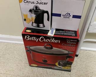 Three boxed small kitchen appliances, including a Pohl + Schmitt Ultimate Citrus Juicer, a Smart Home Ice Crusher, and a Betty Crocker 5.0-quart slow cooker.