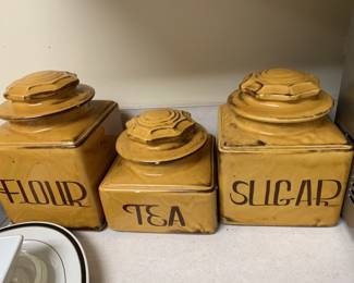 Vintage mid-century ceramic kitchen canister set in a mustard yellow glaze, featuring stylized black lettering for flour, tea, and sugar.