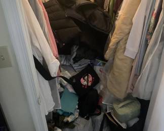 Assorted women's clothing, coats, and bags hanging and piled inside a closet.