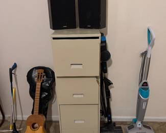 Metal file cabinet, stereo speakers, guitar and stick vacuum