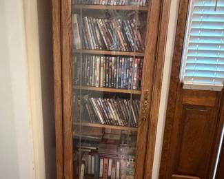 Tall wood cabinet with glass doors holding CD and DVD collection