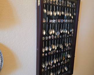 Wall-mounted glass-front shadow box display case filled with a collection of vintage souvenir spoons.