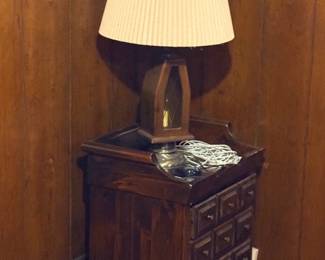 Vintage dark stain wooden nightstand with multi-drawer front design, topped with a lantern-style table lamp featuring a pleated shade.
