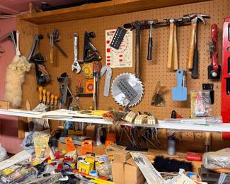 Workshop wall pegboard with assorted vintage hand tools, including hammers, planes, levels, and saw blades, above a cluttered workbench.