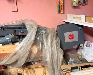 Vintage Shopsmith bandsaw attachment and power tool accessories, stored under plastic sheeting and on shelves in a workshop.