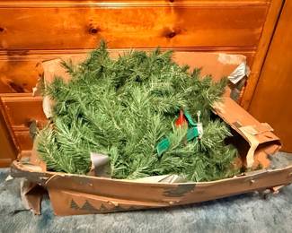 Disassembled artificial Christmas tree branches packed inside a heavily worn, duct-taped cardboard box.