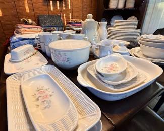 Large collection of vintage floral pattern porcelain dishware, including serving platters, bowls, covered dishes, creamer pitchers, and teacups arranged on a wooden dining table.
