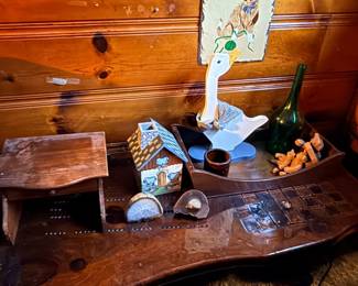 Rustic wooden coffee table displaying decor items including a ceramic house, goose figurine, cut geode halves, and a green glass bottle in a wooden tray.