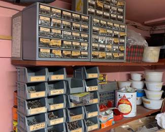 Workshop storage cabinets and open plastic bins filled with sorted hardware, nails, screws, and fasteners.