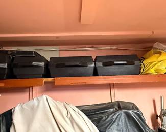 Collection of molded plastic tool cases and storage containers arranged on a high wooden shelf in a workshop.