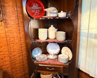 Vintage dark wood corner hutch with scalloped shelving trim, filled with holiday dishware, serving pieces, and glassware.