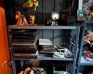 Metal shelving unit filled with various home decor, including stacked picture frames, small plush toys, decorative figurines, and maracas.