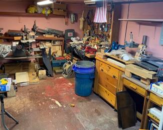 Workshop room filled with power tools, woodworking equipment, wooden cabinets, hand tools, and assorted hardware.
