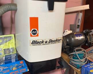 Vintage Black & Decker central vacuum power unit mounted on a wall, surrounded by various workshop tools and accessories.