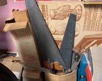 Collection of vintage hand saws stored in a container, surrounded by boxed tools and accessories including a Craftsman router guide.