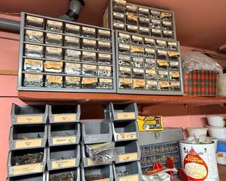 Workshop storage shelves organized with metal small-parts cabinets, plastic stacking bins filled with hardware, and miscellaneous shop supplies.