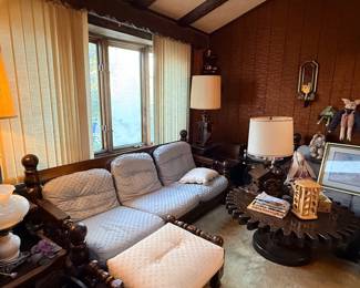 Vintage wood-frame sofa set with patterned blue cushions, paired with a matching ottoman and a unique gear-shaped coffee table in a wood-paneled living room.