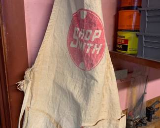 Vintage canvas Shopsmith work apron featuring a printed red graphic logo and front tool pockets, showing heavy wear and staining from age.