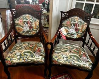 Beautiful matching wooden armchairs featuring decorative inlay, carved details, curved arms, and colorful scenic upholstery.