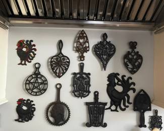 Collection of decorative metal trivets and wall pieces featuring roosters, hearts, geometric designs, and other traditional motifs.