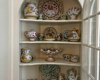 Colorful collection of Italian ceramic plates, pitchers, covered jars, serving bowls, mugs, and decorative pottery featuring traditional painted designs.