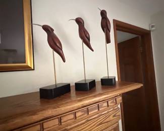 Trio of mid-century modern carved wooden bird sculptures on metal stands with black rectangular bases.