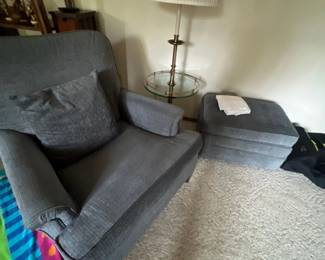 Gray upholstered armchair with matching throw pillow and ottoman, paired with a brass and glass floor lamp table.
