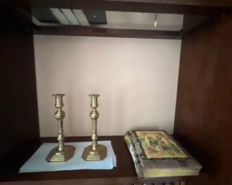 Pair of vintage brass baluster-style candlesticks displayed on a shelf alongside a decorative book featuring a portrait cover illustration.