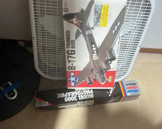 A collection of household items including a vintage white box fan, a Lindberg B-17G Thunderbird model airplane kit, and a boxed Albinar Model 3000 photographic tripod.