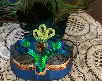 Venetian-style masquerade mask featuring blue fabric, iridescent sequin trim, and peacock feather plumage.