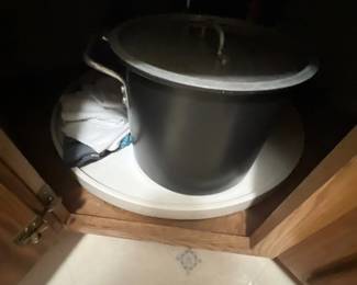 Large dark metal stock pot with a fitted lid, resting inside a corner Lazy Susan cabinet.