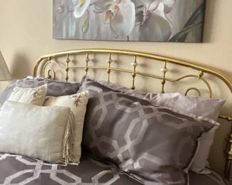 Brass queen headboard with spindle accents, staged with geometric patterned bedding and a large floral canvas print above.